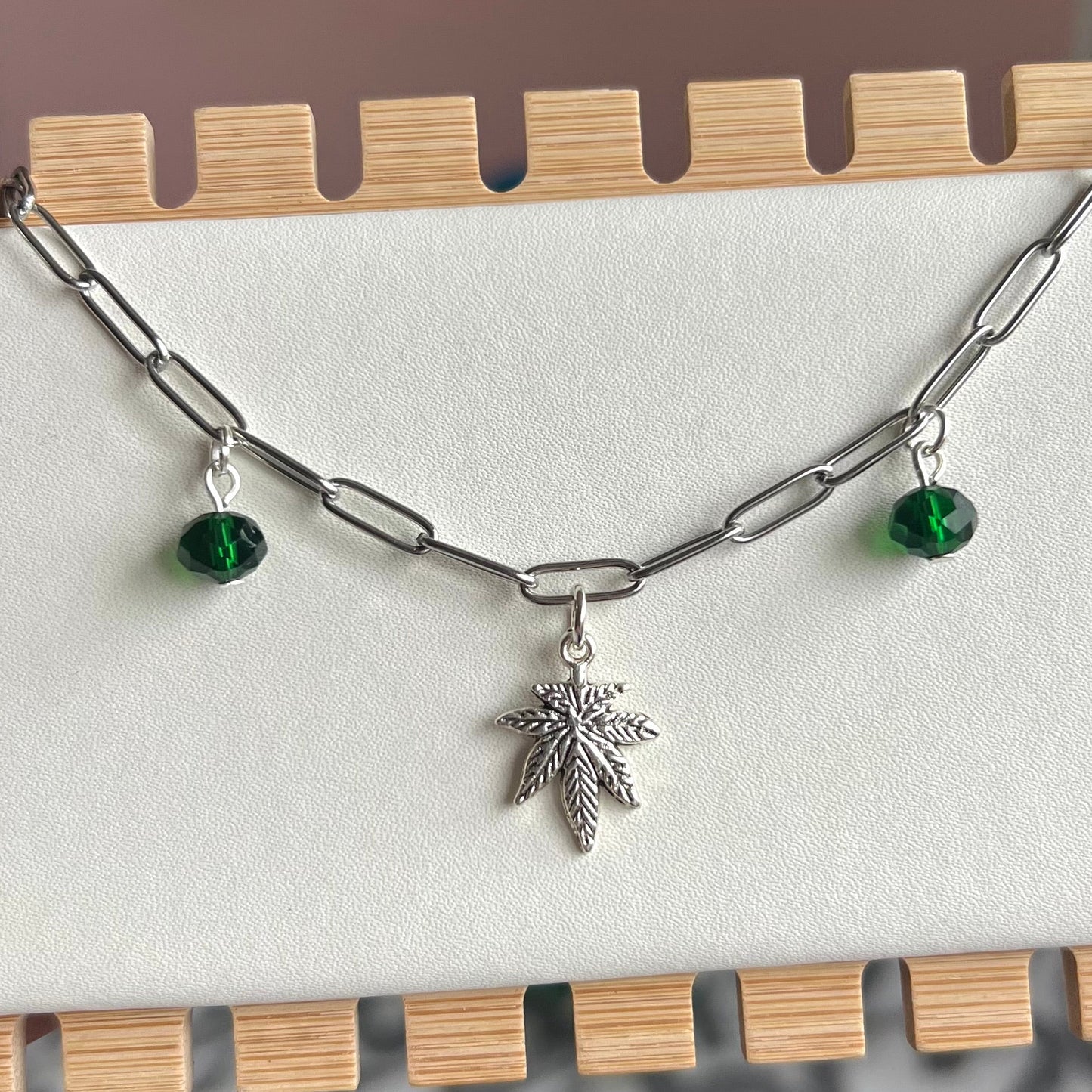 Necklace with leaf charm and green beads on a wooden stand