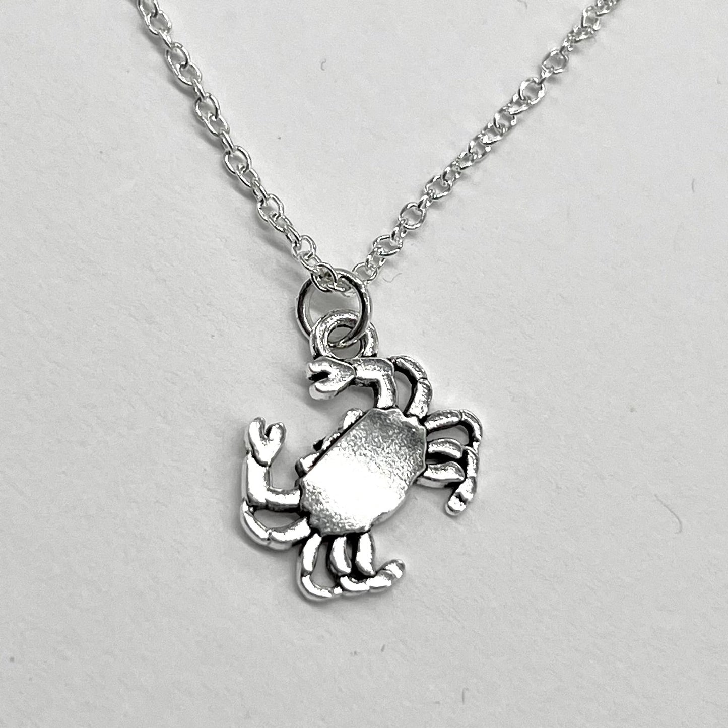 A silver crab charm on a sterling silver chain against a white background.