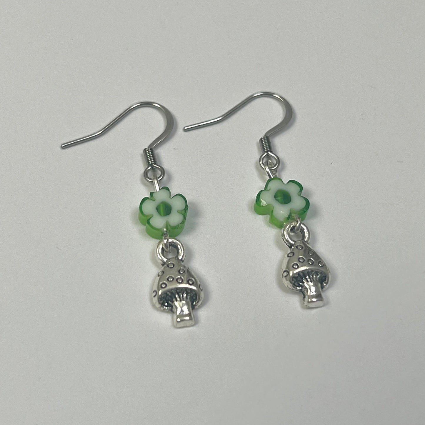 Pair of silver earrings with green floral and mushroom charms on a light gray background